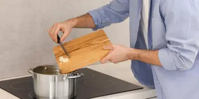 A man adds chopped garlic to a pot on an induction stove.