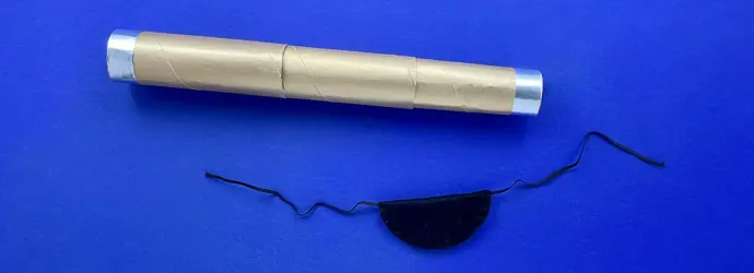 A homemade gold cardboard telescope next to a black DIY pirate eye patch on a blue background