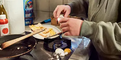 Woman with shocked expression cooking drops egg on the stove, missing the pan.