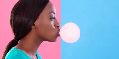 Woman blowing a chewing gum bubble against a pink and blue background