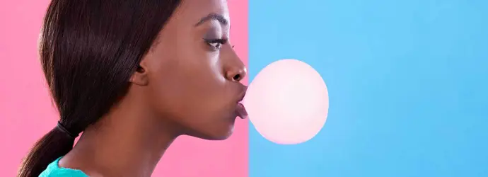 Woman blowing a chewing gum bubble against a pink and blue background