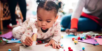 A little girl holding a glue stick while doing arts and crafts