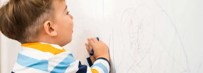 Baby boy writing on a clean wallpaper with crayons