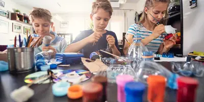 3 children learning how to reduce waste by making crafts from recyclable plastics and cardboard tubes