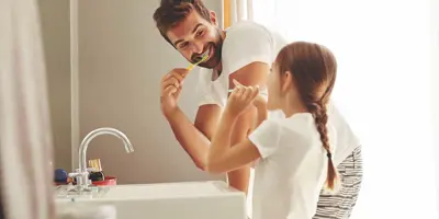 A man and his young daughter learning how to save water whilst brushing their teeth together in a bathroom