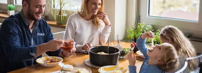 A family sitting around a table having dinner while kids are playing and messing around with food