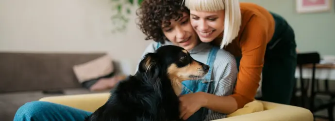 Two women and a dog snuggle on a mustard yellow couch.