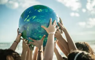 A group of children hold up an Earth-like globe into the air.