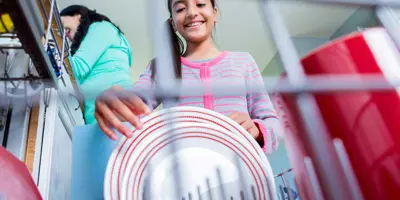 A girl helping her mother in the kitchen loading or unloading the dishwasher