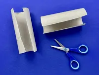 Two halves of cardboard tubes have been cut lengthwise and are on a blue table next to open scissors.