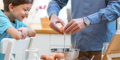 A man and a child joyfully crack eggs into a mixing bowl.