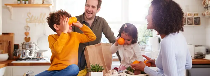 Two kids play with oranges; parents unpack groceries.