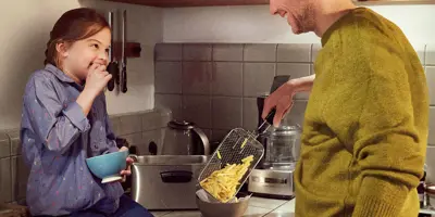 Dad and daughter in the kitchen preparing a meal for the family with french fries.
