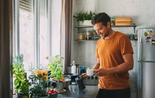 A man smiles while making a coffee in his kitchen.