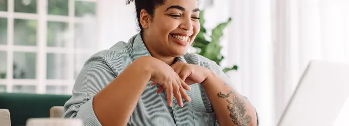 A woman smiles brightly at a laptop open in front of her.