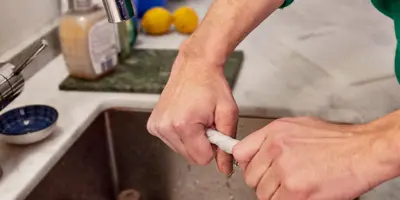 Hands of a person wearing green jumper cleaning the kitchen sink wringing out a wet kitchen towel.
