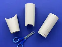 3 cardboard tubes are on a blue surface with the ends cut to the animal shapes with a pair of scissors below them.