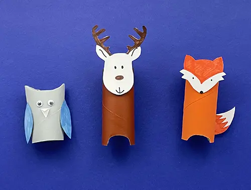 The completed grey owl, brown reindeer and orange fox cardboard tube animals are on a blue surface together.