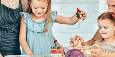 Two children joyfully helps two adults cook, stirring ingredients in a bowl.