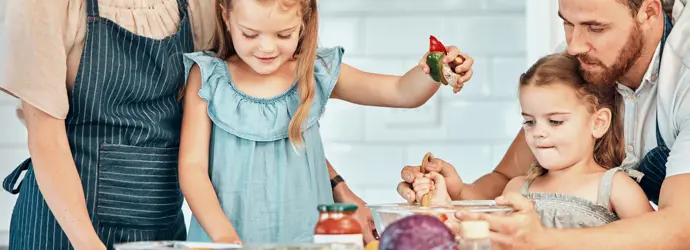 Two children joyfully helps two adults cook, stirring ingredients in a bowl.