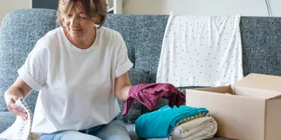 A woman sorts clothing into a box in a cozy living room.