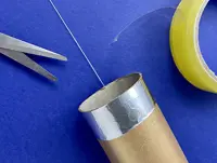 A close up of one end of the DIY telescope, with the string through the middle next to scissors and a roll of tape.