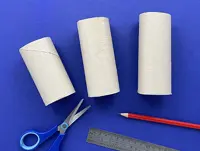 3 different size cardboard tubes are on a blue surface above a metal ruler, red pencil, and pair of blue scissors.