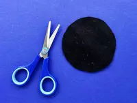 A black circle of fabric is laid on a blue surface next to a pair of blue handled scissors.