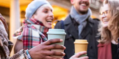 Laughing friends hold coffee cups outside.