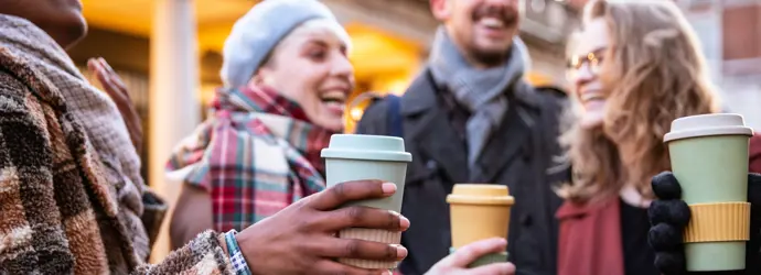 Laughing friends hold coffee cups outside.