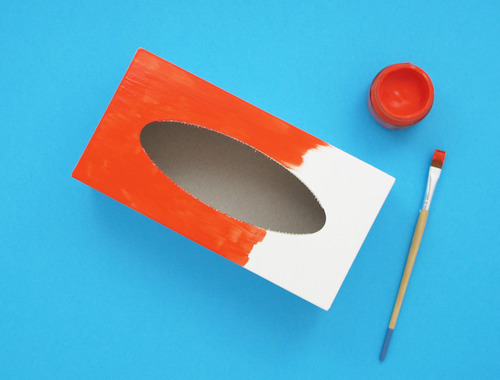 An empty tissue box with paint and a paintbrush to make a homemade instrument.