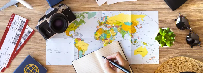 A person planning a trip at a wooden table with a map of the world, passport and tickets.