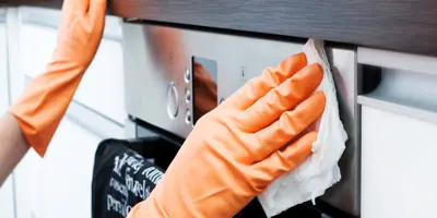 A person wearing gloves cleans the exterior of an oven