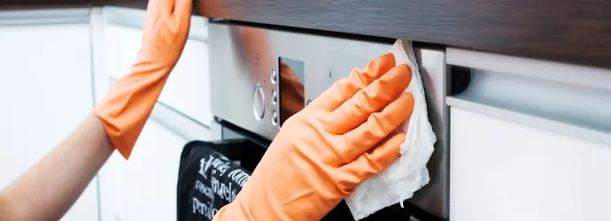 A person wearing gloves cleans the exterior of an oven