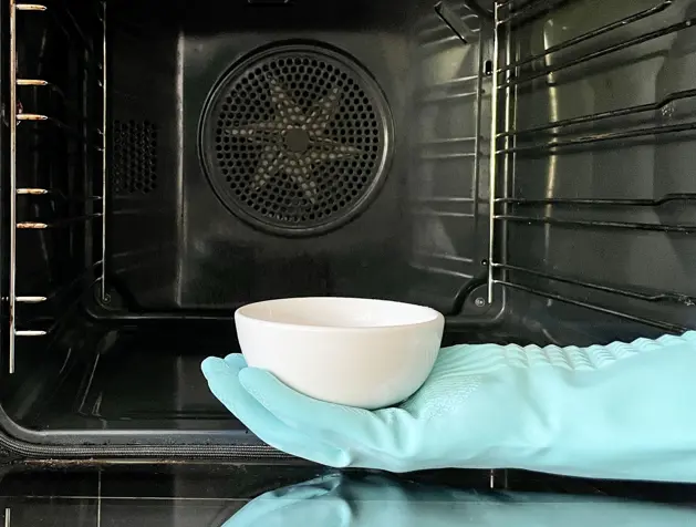 Young woman in apron cleaning the oven with spray and cloth