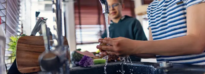 Boys rinse fresh veggies under tap in a modern kitchen.