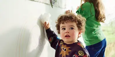 Two kids doodling on the hard surface with crayons, leaving pen stains.
