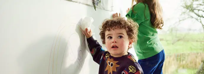 Two kids doodling on the hard surface with crayons, leaving pen stains.
