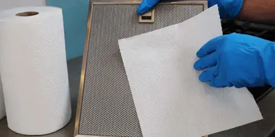 Woman in rubber gloves cleaning cooker hood in kitchen